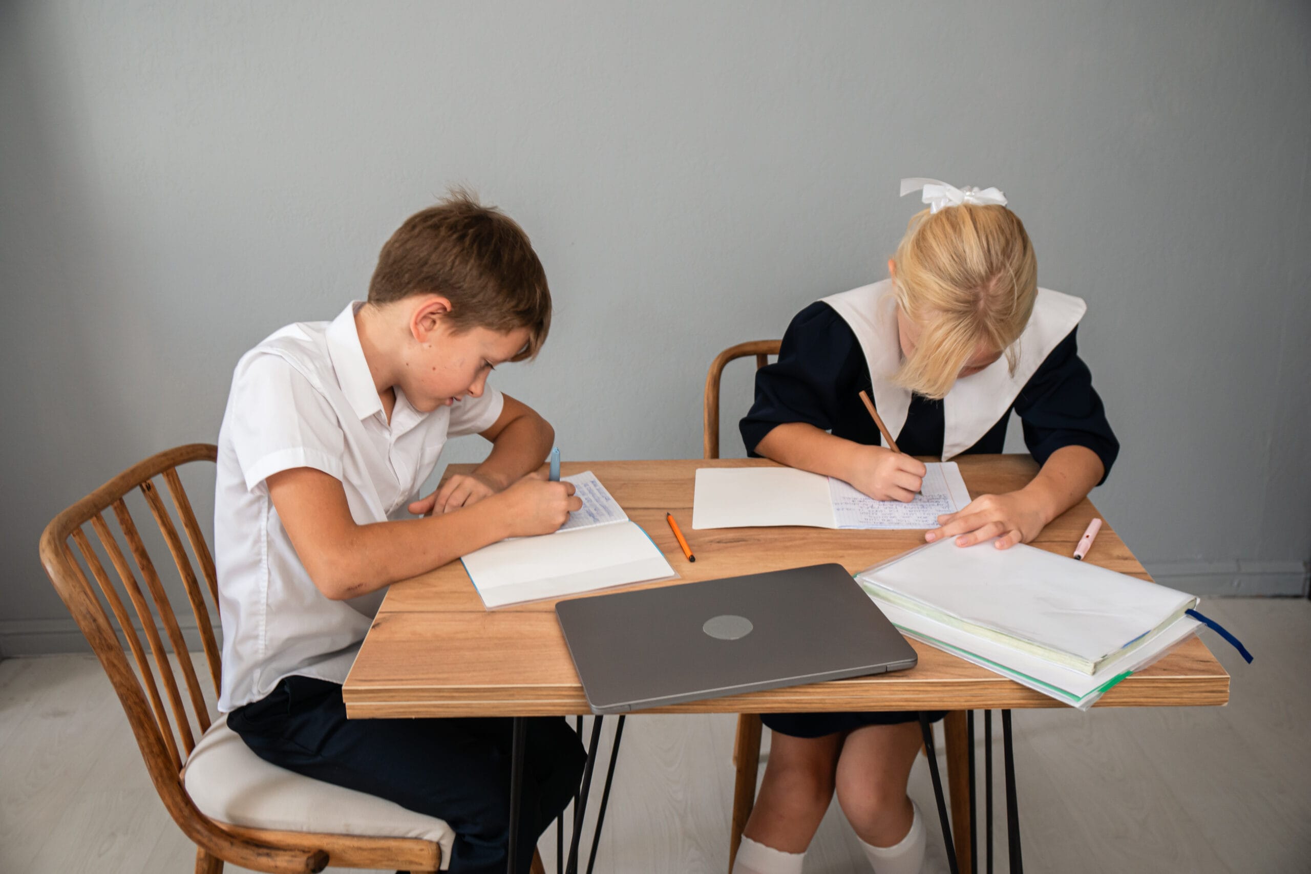 Two elementary school kids in uniforms doing homework together at a table